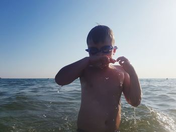 Full length of shirtless boy in sea against clear sky