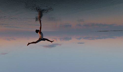 Side view of man in water against sky during sunset