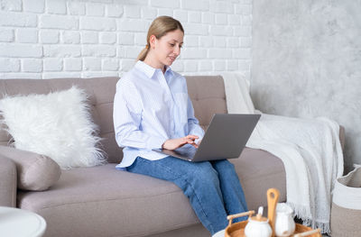 Smiling woman using laptop while sitting on sofa