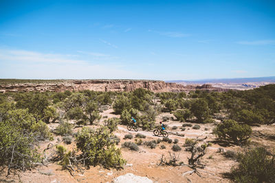 High angle view of couple riding bicycles amidst trees on landscape against blue sky