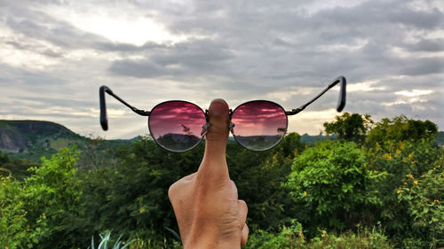 Cropped hand holding eyeglasses against sky