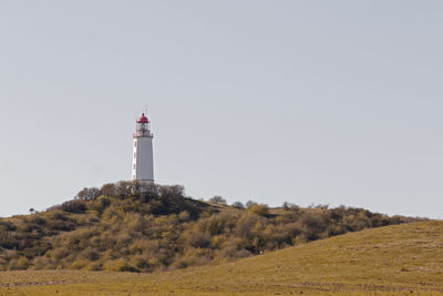 Lighthouse on field by building against clear sky