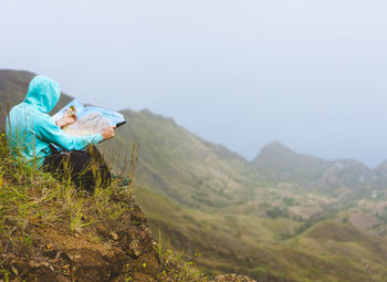 Man reading map while sitting on mountain