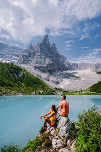 Man sitting by lake against sky