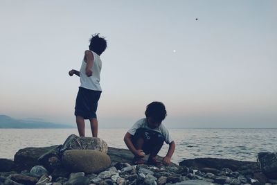 Boys throwing stone in sea against sky