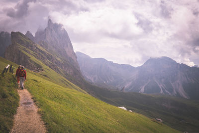 Rear view of hikers walking on mountain against cloudy sky