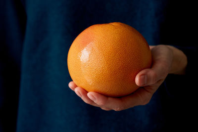 Close-up of woman's hand holding whole red bright citrus fruit grapefruit on dark 