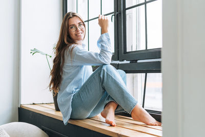 Portrait of young woman sitting on window