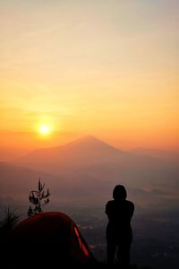 Woman standing by tent against mountains during sunset