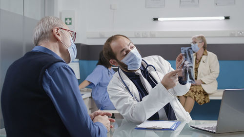 Doctor discussing over x-ray with patient in medical clinic during pandemic
