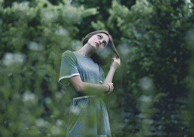 Woman looking away while standing against trees