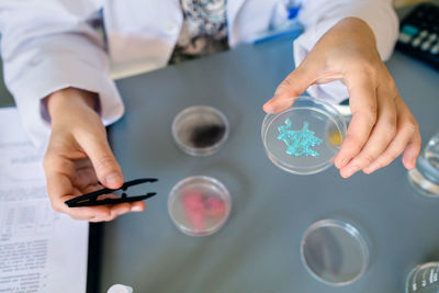 Unrecognizable female scientist showing blue glitter in facial cream sample over petri dish on lab