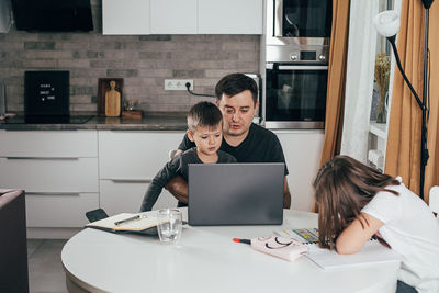 Father working on laptop while daughter studying at home