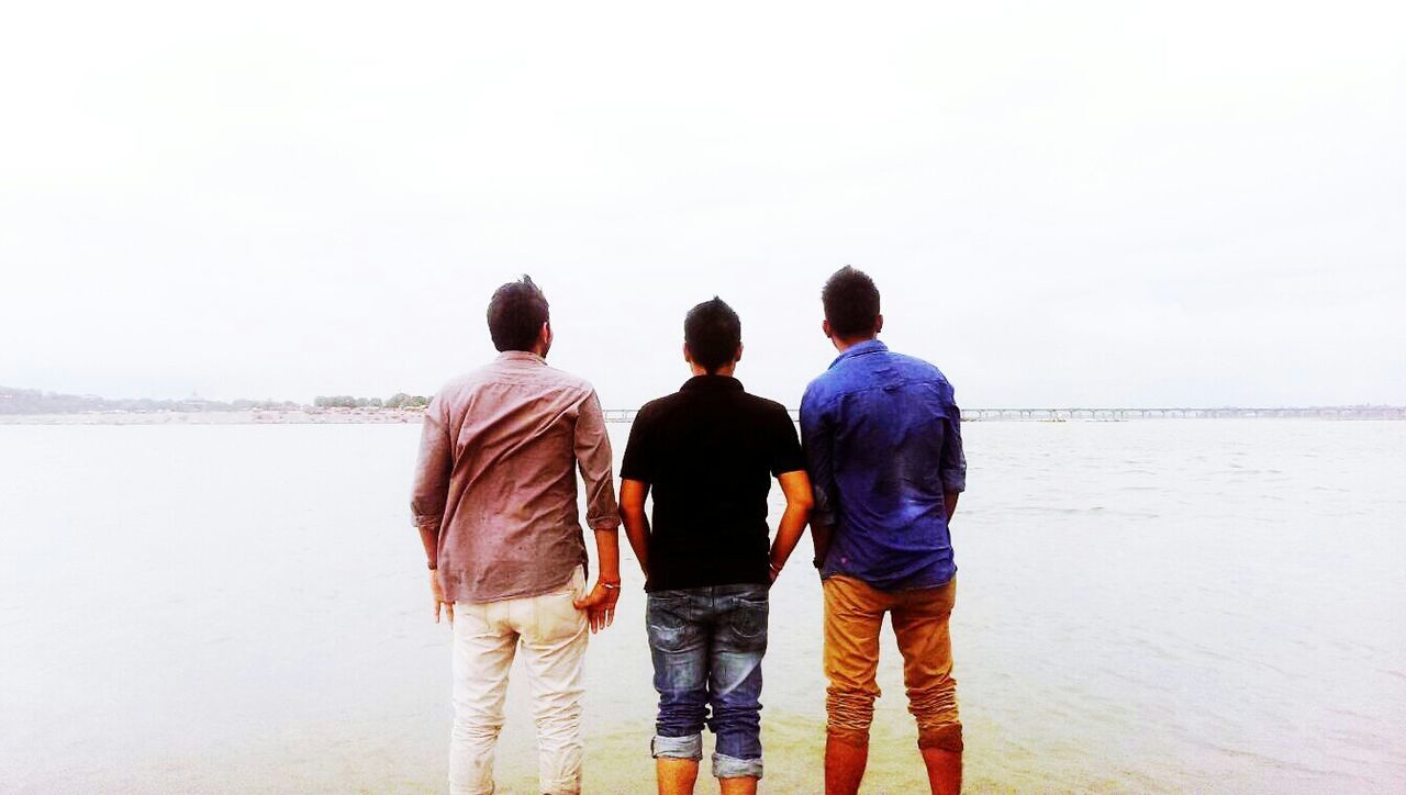 rear view, togetherness, men, clear sky, lifestyles, copy space, standing, bonding, leisure activity, casual clothing, water, person, sea, love, friendship, full length, boys