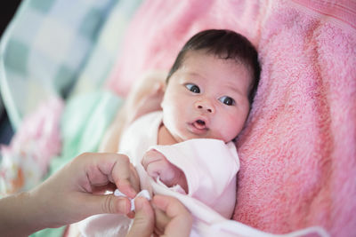 Cropped hands of mother with newborn daughter on bed
