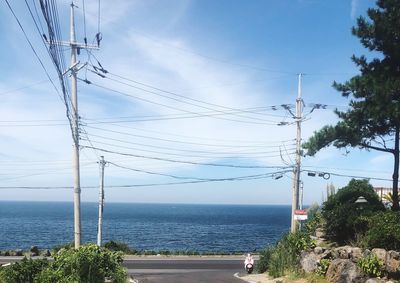 Electricity pylon by sea against sky