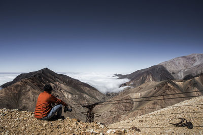 Man sitting on mountain against clear sky