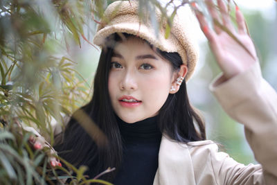 Portrait of beautiful young woman standing by tree during winter