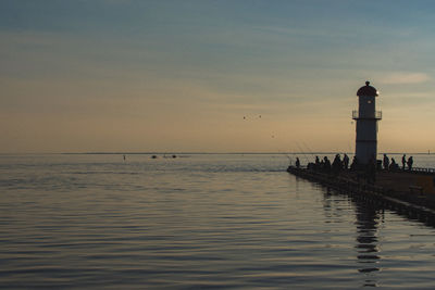 Lighthouse by sea against sky during sunset