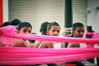 Boys looking away while sitting on footpath amidst pink fabric