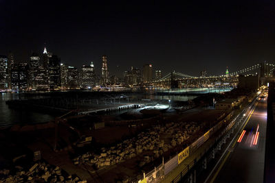 Illuminated bridge over river by buildings against sky at night