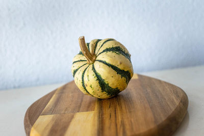 A cream and green mini pumpkin standing on a wooden chopping board
