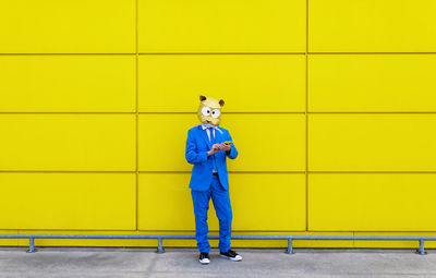 Full length portrait of man standing against yellow wall