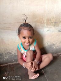 Portrait of smiling girl sitting against wall