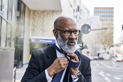 Mature businessman tying tie in the street