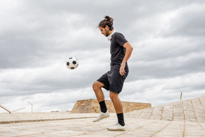 Man training with soccer ball against cloudy sky