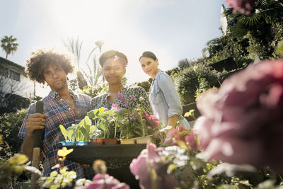 Portrait of smiling friends holding potted plants in community garden