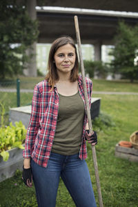 Portrait of mid adult woman holding rake in community garden