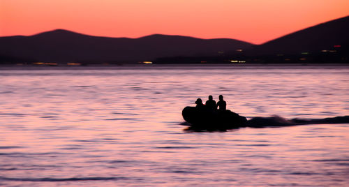 Silhouette people on boat over lake at dusk