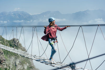 A happy cheerful woman walks on a suspension bridge high in the mountains 