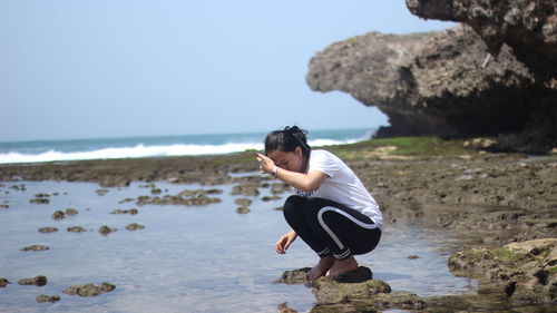 Side view of man on rock at beach against sky