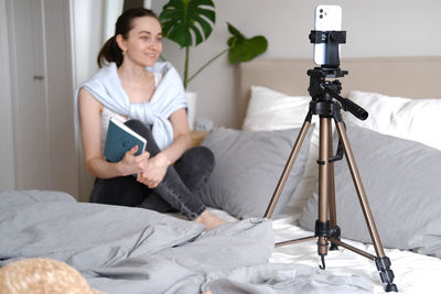 Rear view of woman using mobile phone while sitting on bed at home