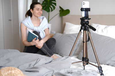 Rear view of woman using mobile phone while sitting on bed at home