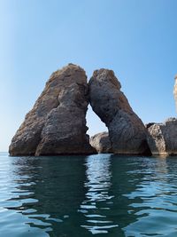 Rock formation in sea against clear blue sky