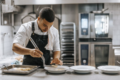 Young male chef plating dumpling with spatula on kitchen counter in restaurant