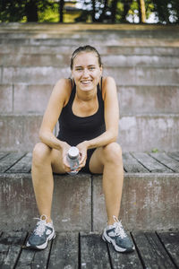 Portrait of smiling woman holding water bottle while sitting on steps