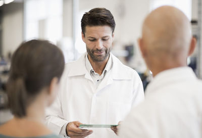 Engineer looking circuit board with business people in foreground at manufacturing plant