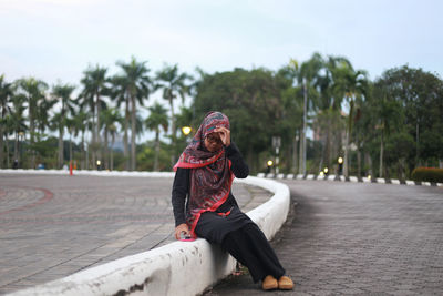 Thoughtful young woman sitting on dividing line at street