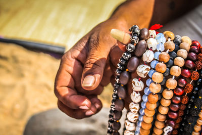 Cropped hands of man selling bead necklaces at beach