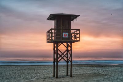 Lifeguard hut on beach against sky during sunset