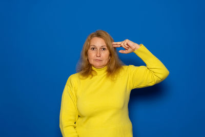 Portrait of young woman standing against blue background