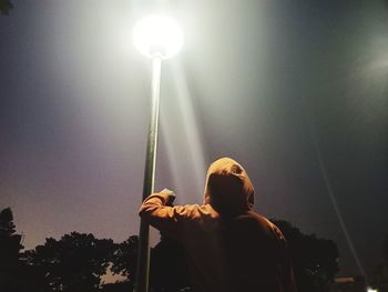 Rear view of man looking at illuminated lamp against sky at night