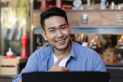 Portrait of smiling male owner showing thumbs up sign at cafe