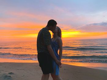 Couple kissing at beach against sky during sunset