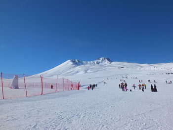 People on snowcapped mountain against clear blue sky