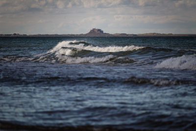 Waves rushing towards shore against sky